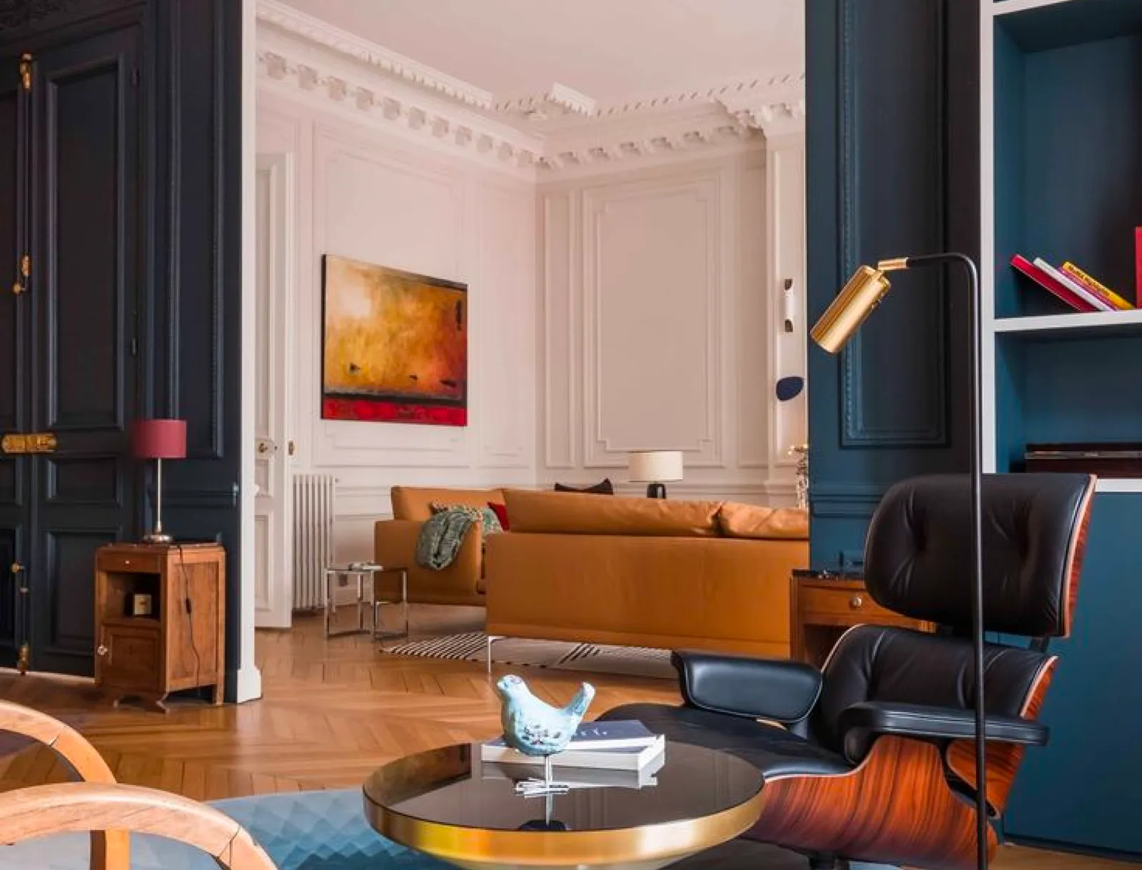 Appartement haussmannien à Paris avec moulures, boiseries bleu nuit, canapé en cuir camel et parquet en point de Hongrie