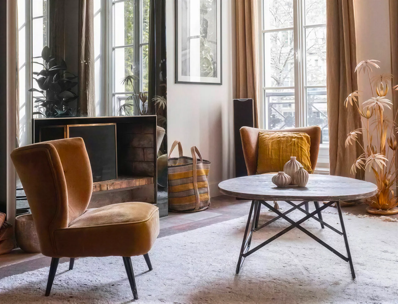 Salon lumineux d’un appartement parisien avec fauteuils en velours ocre, table basse ronde et grandes fenêtres sur balcon