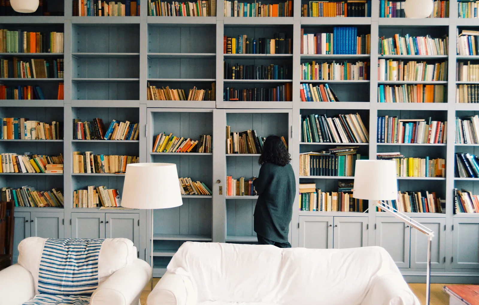 Femme choisissant un livre dans une grande bibliothèque du sol au plafond, dans un salon lumineux